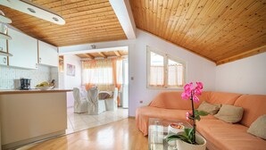 Amplia sala de estar con techo de madera, un sofá, una mesa de centro de vidrio y una zona de cocina con juego de comedor.