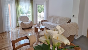A cozy living room with a sofa, armchair, and coffee table. There is a window with sheer curtains and a view of greenery outside. - House Bella Vista (Vinodol)