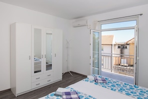Ein Schlafzimmer mit großem Kleiderschrank, einem Bett mit blau-weißer Blumenoptik und einem Balkon mit Blick auf Gebäude.