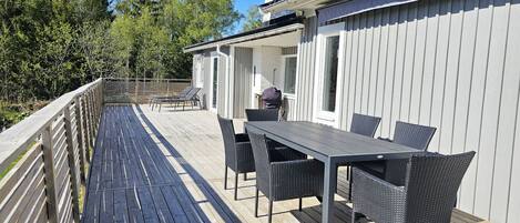 A wooden deck with a table and chairs, a covered outdoor area, and a white building with vertical siding.