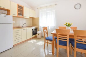 Eine moderne Küche mit Kühlschrank, Herd und Spüle. Ein Esstisch mit Stühlen und eine Vase mit Blumen sind ebenfalls vorhanden.