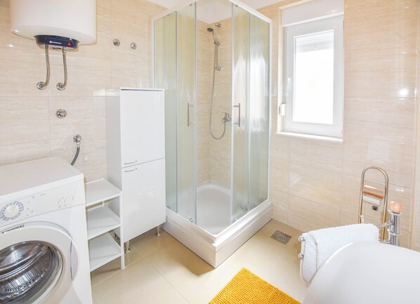 A modern bathroom with a glass-enclosed shower, a built-in washing machine, and a toilet with a towel rack. - Apartment Jadranka (Biograd na Moru)