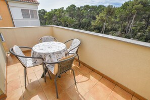 Ein Balkon mit rundem Tisch, vier Stühlen, gefliestem Boden und Blick auf Bäume.