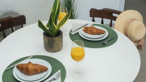 Uma mesa de jantar redonda com um vaso de planta, duas travessas com croissants, um copo de sumo de laranja e um chapéu de palha.