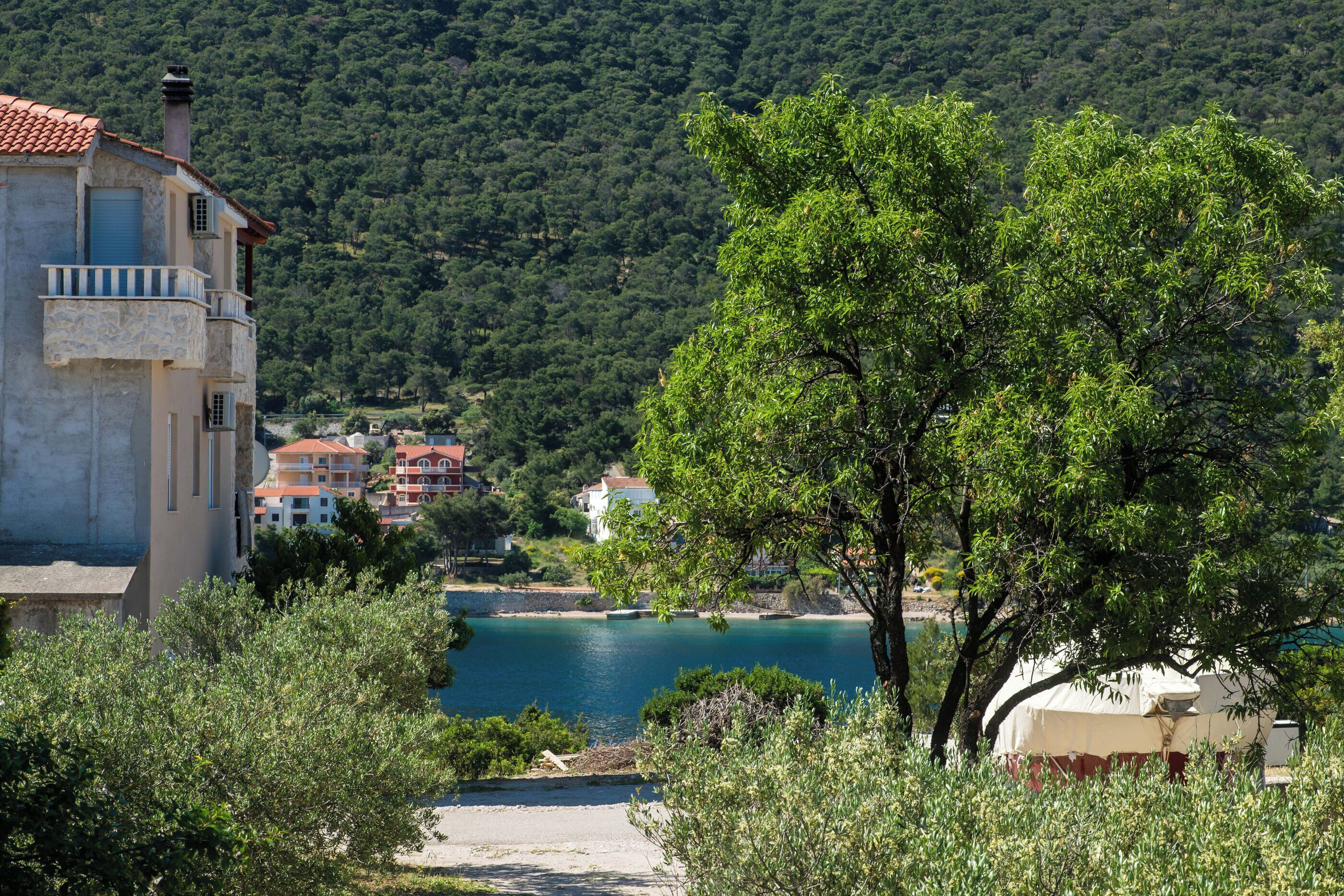 A coastal building with a balcony, surrounded by lush greenery and a view of the sea.