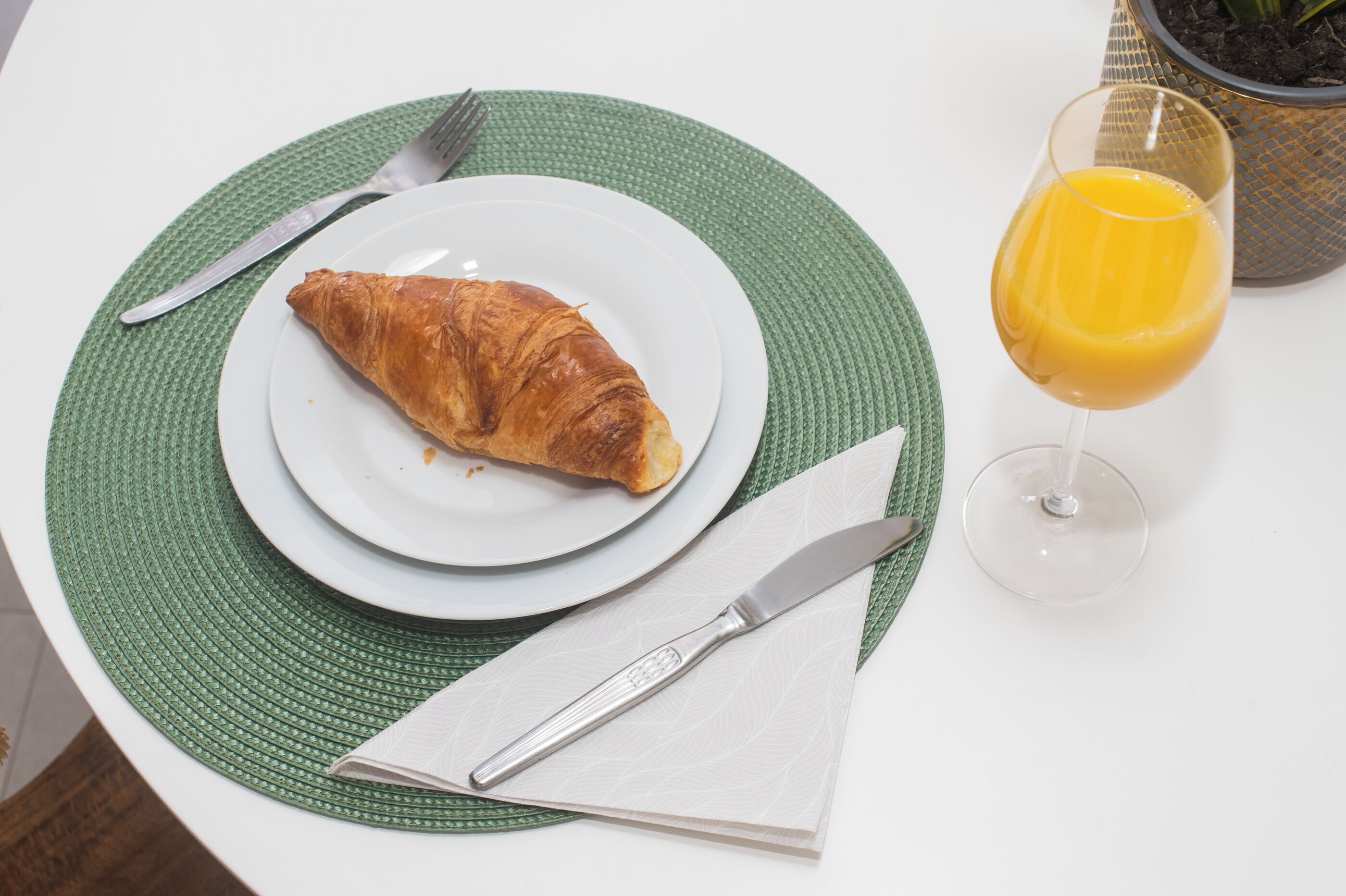 A plate with a croissant, a glass of orange juice, and cutlery on a table with a green placemat.