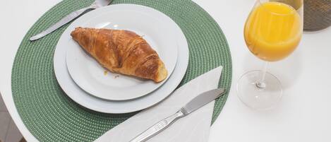 A plate with a croissant, a glass of orange juice, and cutlery on a table with a green placemat.