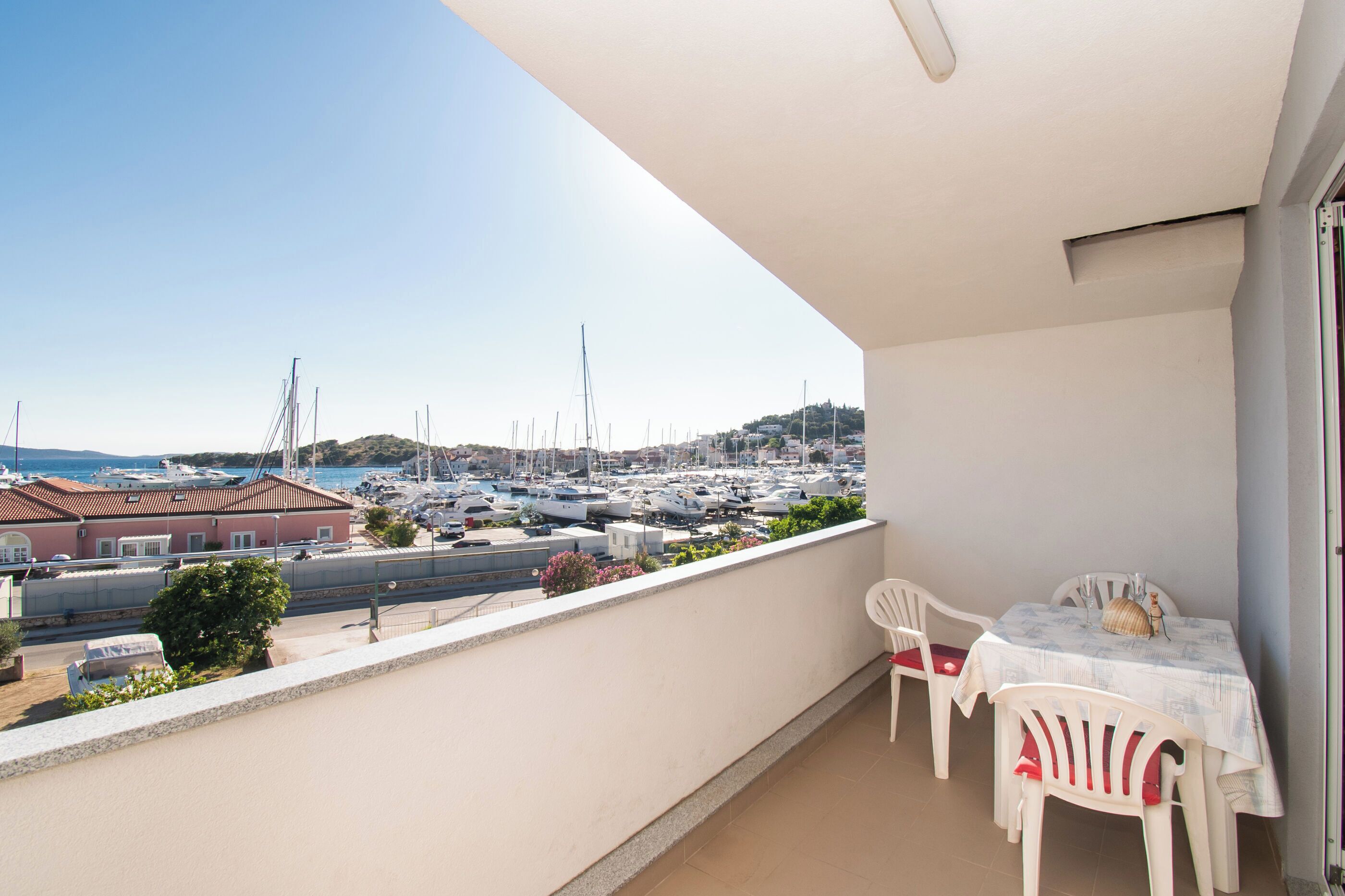 Un balcon donnant sur un port de plaisance, avec des chaises blanches et une table agrémentée d’un objet décoratif.