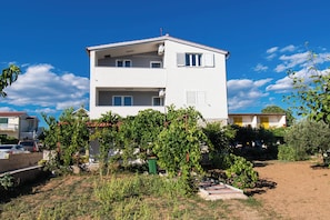 A two-story white building with balconies, surrounded by greenery and a clear blue sky. - Apartments Nena (Tribunj)