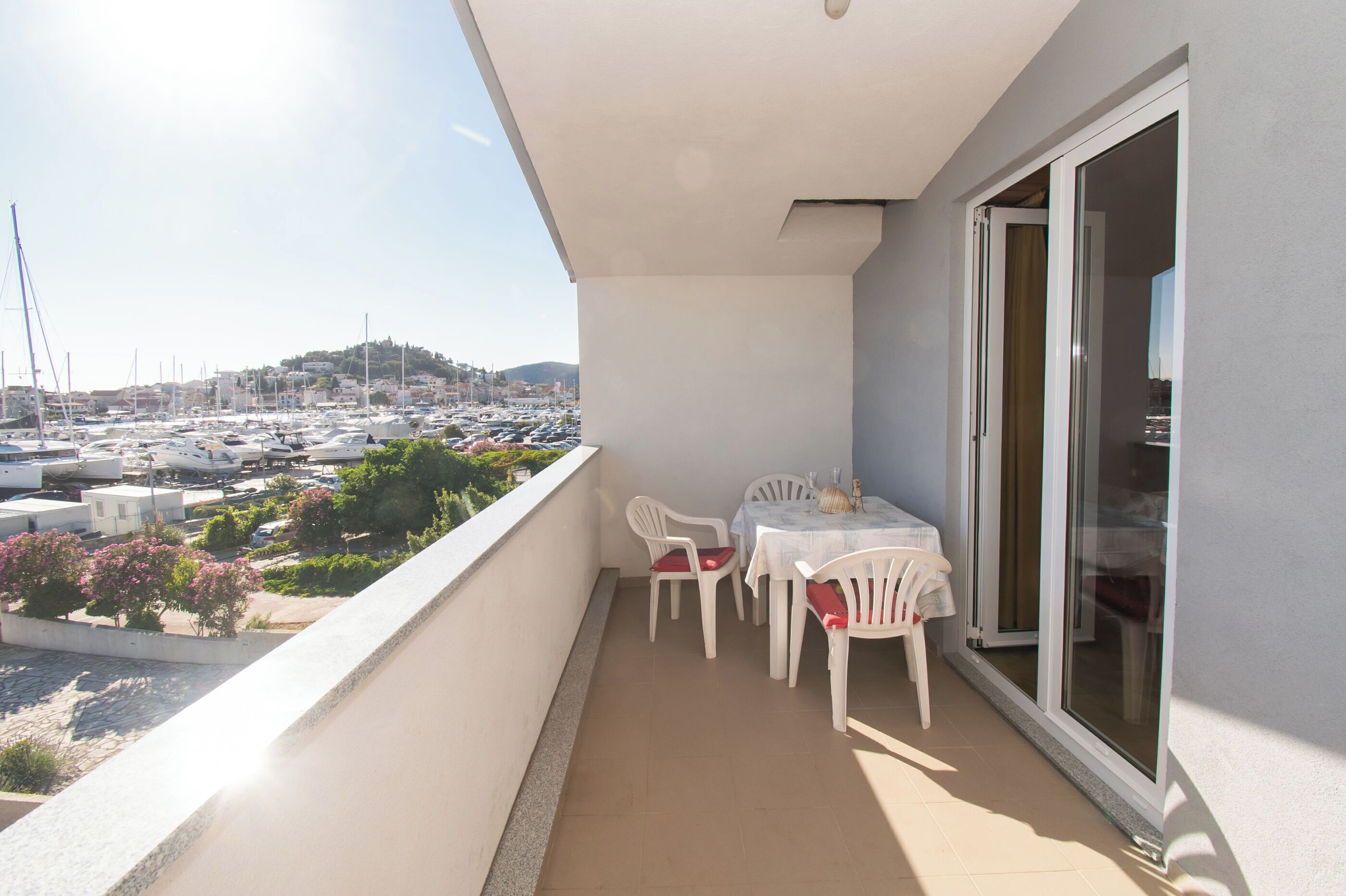A balcony with a table and chairs, overlooking a marina with boats and a hilly landscape.