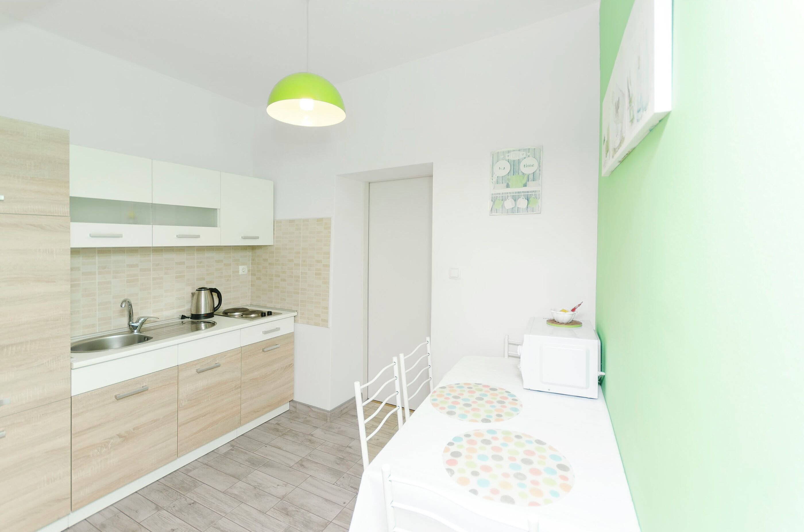 A modern kitchen with white cabinets, a sink, and a microwave. There is a green pendant light above the counter.