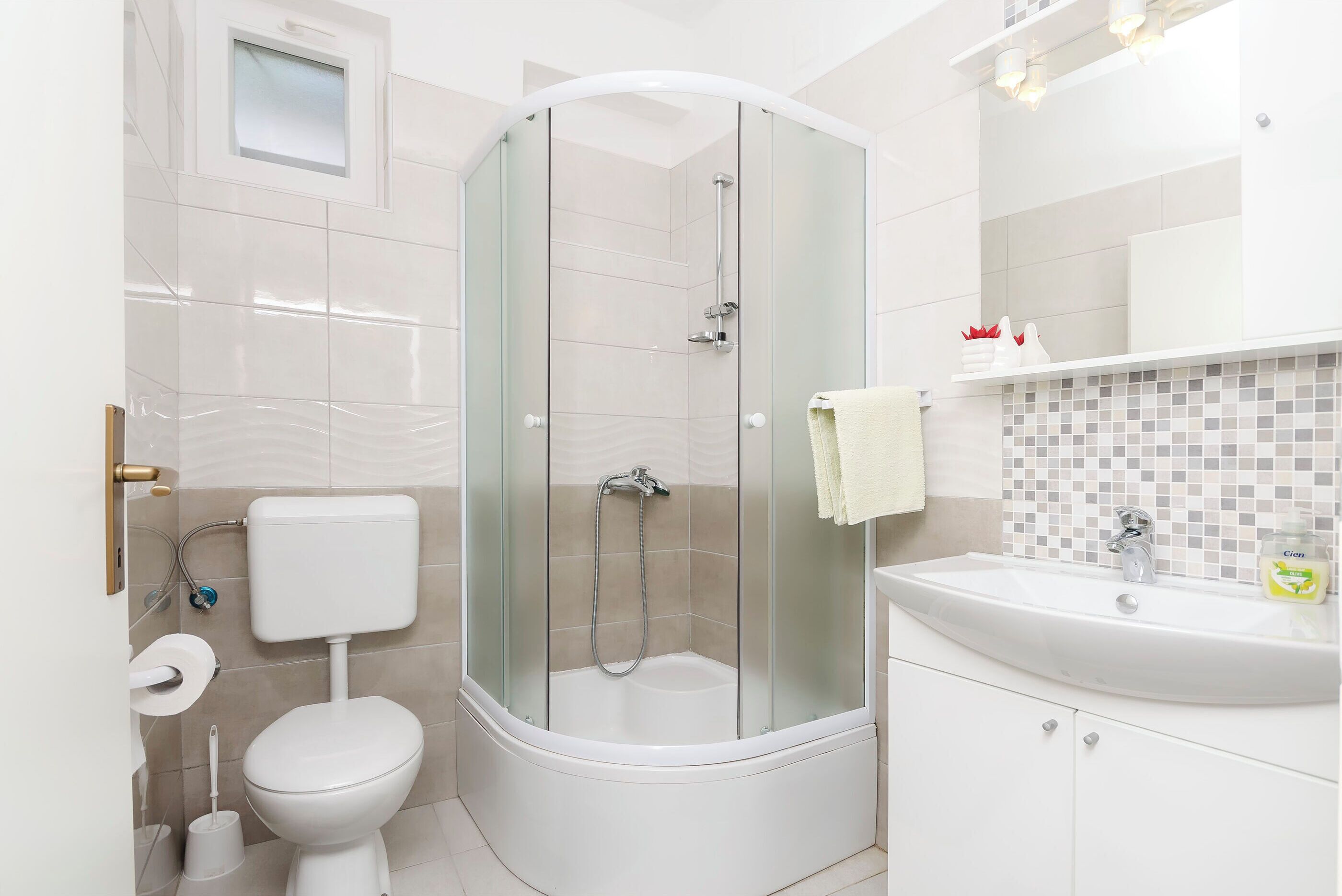 A modern bathroom with a glass-enclosed shower, a toilet, and a sink with a mirror above.