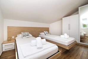 Ein modernes Hotelzimmer mit zwei Betten, einem Holz-Kopfteil, einem kleinen Nachttisch mit Lampe und einem großen Kleiderschrank.