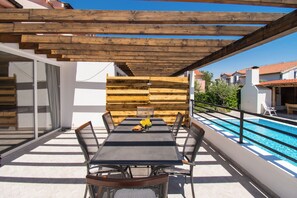 Ein überdachter Essbereich mit Pool im Hintergrund.