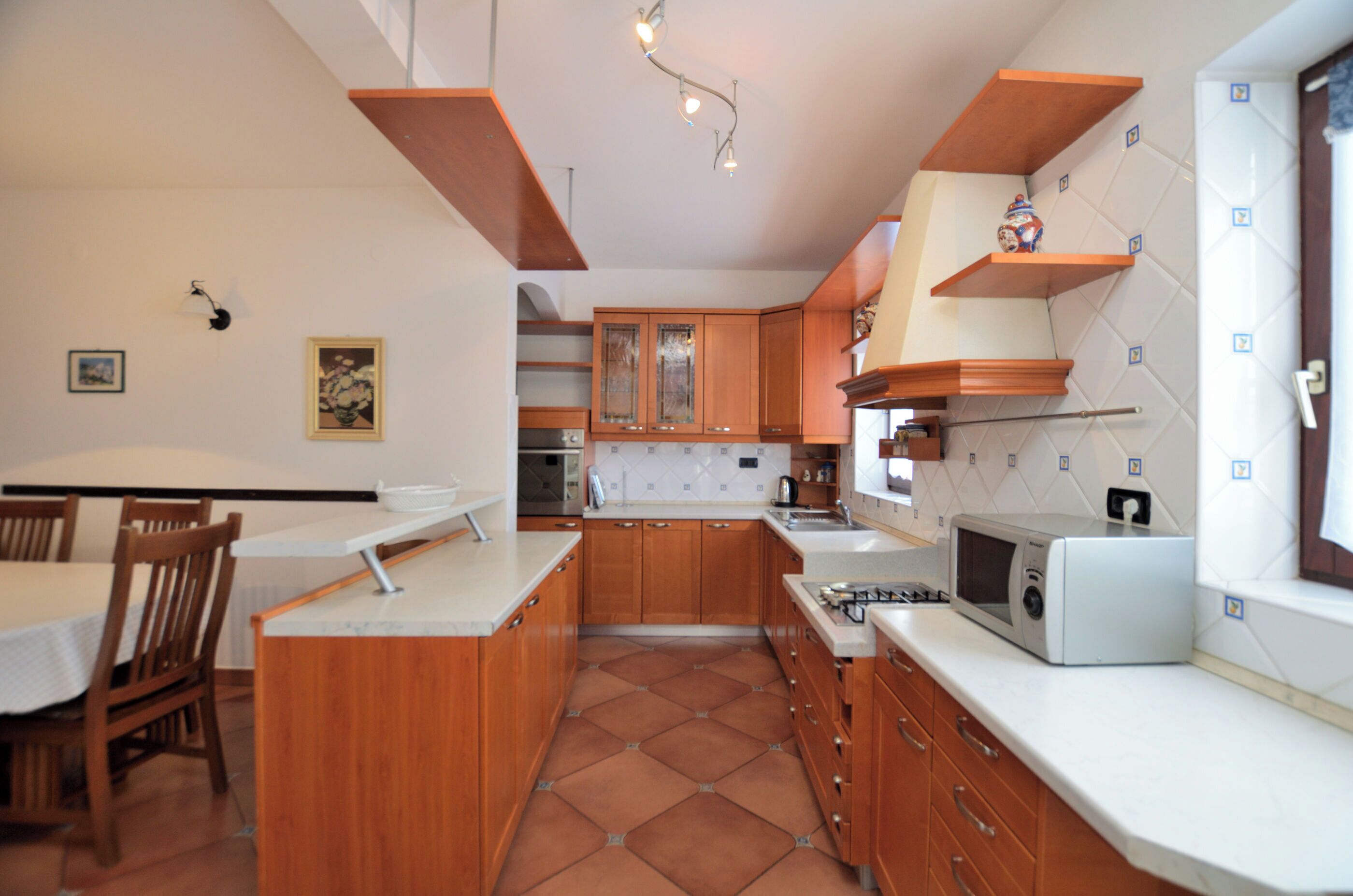 A kitchen with wooden cabinets, a microwave, and a dining area with chairs and a table.