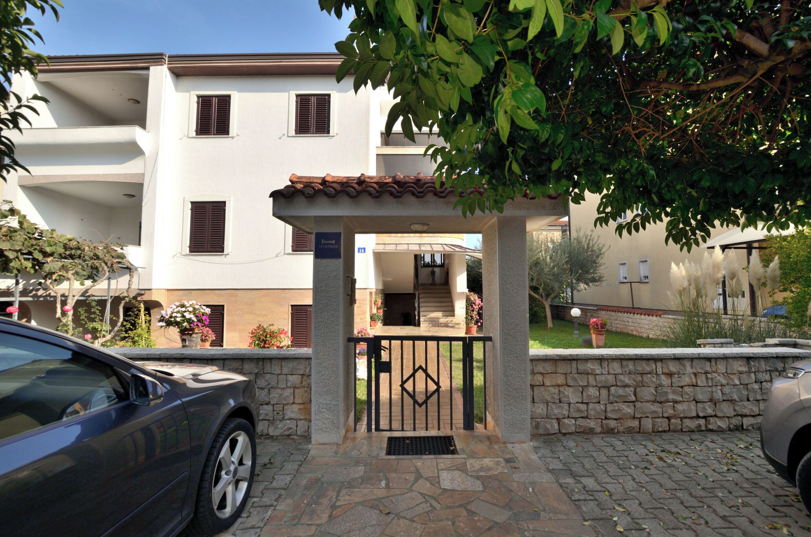 A gated entrance to a building with a stone wall, a covered porch, and a car parked nearby.