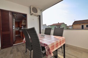 En balkon med bord og stole, en aircondition og udsigt til omkringliggende huse.