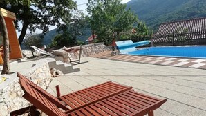 Un espace aménagé au bord de la piscine, avec un fauteuil de relaxation en bois, un mur en pierre et une vue sur une montagne.