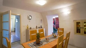 Un coin repas avec une table en bois, des chaises et un ananas en guise de décoration centrale. Il y a une horloge au mur et une porte qui donne sur une autre pièce.