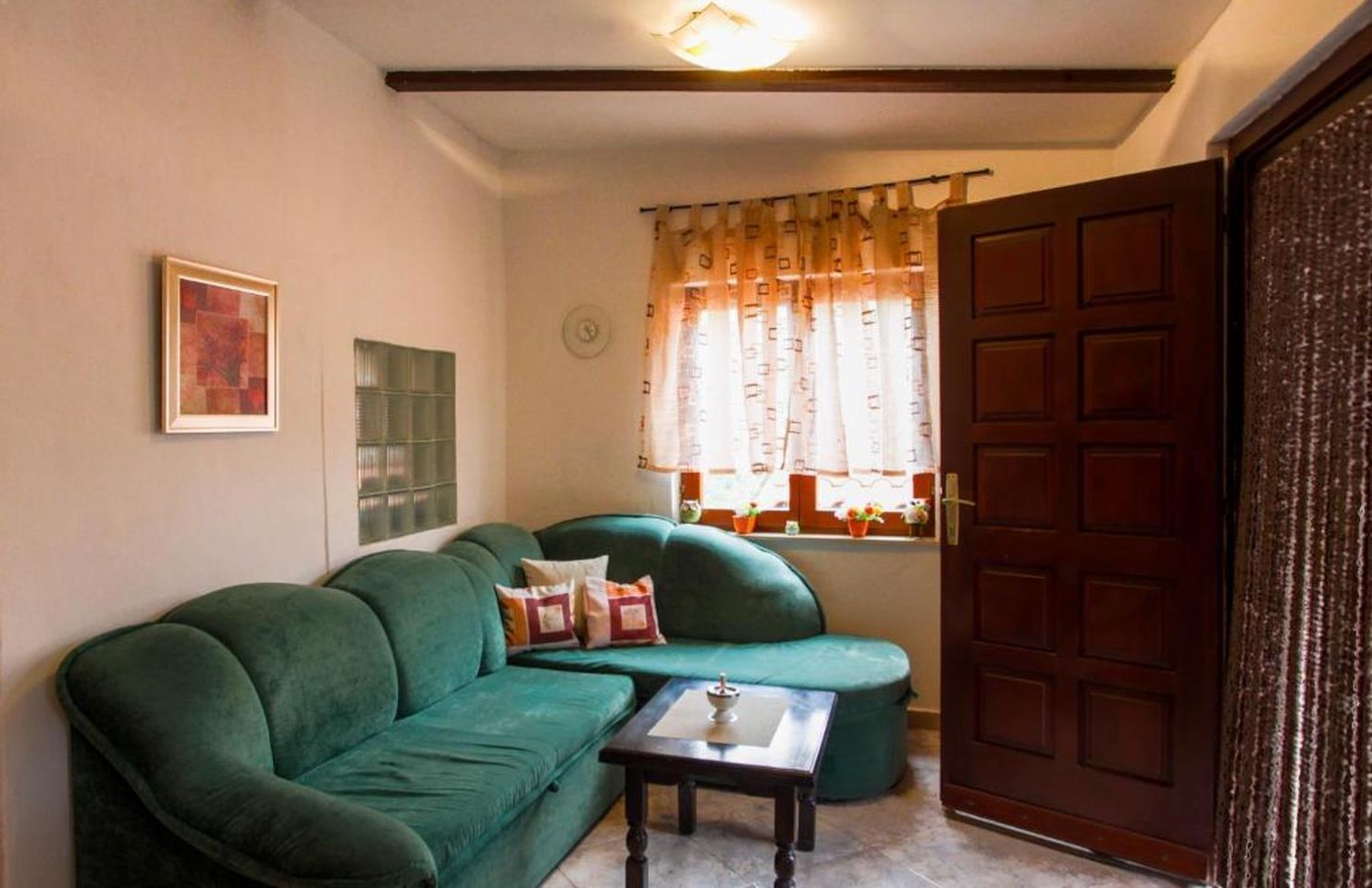 A living room with a green sofa, a small table, a window with curtains, and a wooden door.