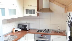 A compact kitchen with white cabinets, a microwave, a stove, and a sink. - House Golovik (Moscenicka Draga)
