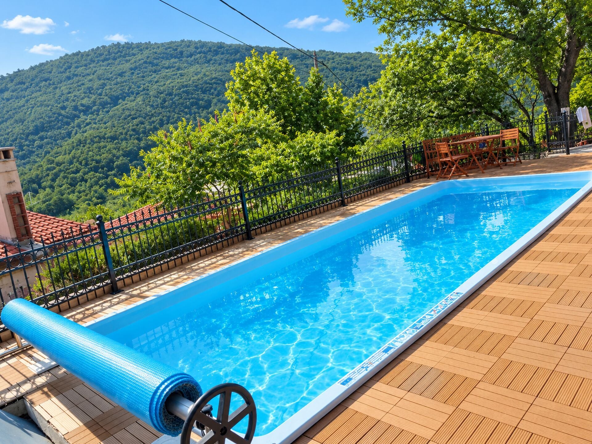 A swimming pool with a wooden deck, surrounded by a metal fence, and a mountainous landscape in the background.