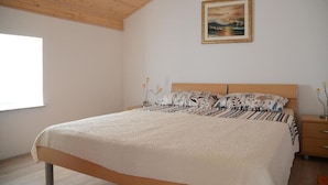 Une chambre avec un plafond en bois, un lit recouvert d’une literie à motifs, une table de chevet avec une lampe et un tableau accroché au mur.