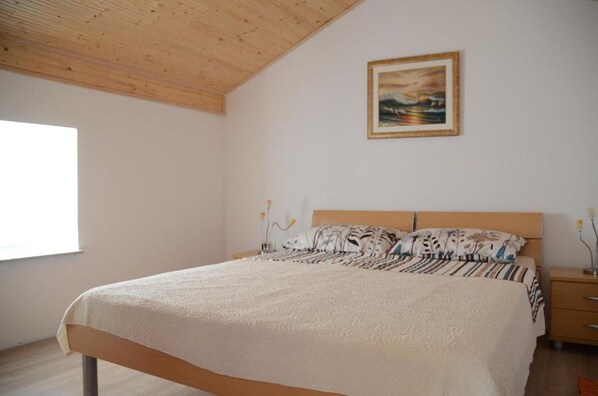 A bedroom with a wooden ceiling, a bed with patterned bedding, a bedside table with a lamp, and a painting on the wall. - House Golovik (Moscenicka Draga)