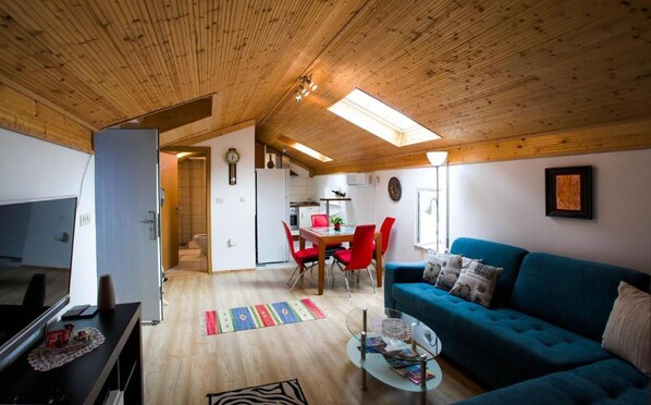 A cozy living room with a blue sofa, a glass coffee table, and a dining area with red chairs. - House Golovik (Moscenicka Draga)