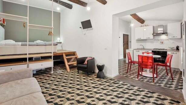 Un espacio habitable compacto con una cama, un escritorio pequeño, una silla y un área de comedor con sillas rojas.