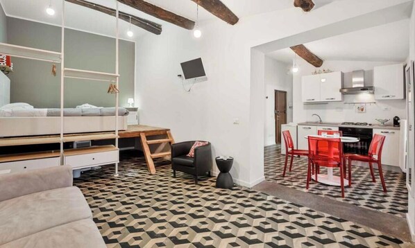 Un espace de vie compact comprenant un lit, un petit bureau, une chaise et un coin repas avec des chaises rouges.