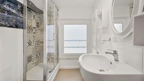 Un baño moderno con una bañera grande, un box de ducha de vidrio y vistas al mar a través de una ventana.