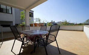 A covered outdoor patio with a round table and four chairs, surrounded by potted plants and a view of neighboring buildings. - Apartments Natasa (Rovinj)