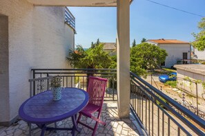 Ein Balkon mit Tisch, Stuhl, einer Topfpflanze und Blick auf eine Wohngegend mit Auto und Bäumen.