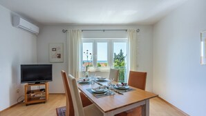 Un comedor con una mesa dispuesta para cuatro, un televisor sobre un mueble bajo y una ventana que ofrece vistas a zonas verdes y edificios.
