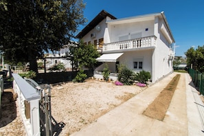 A two-story building with a balcony, a paved driveway, and a landscaped garden with various plants and flowers. - Apartments Lily (Privlaka)