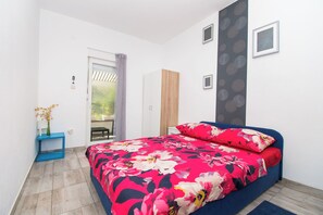 A bedroom with a bed, a wardrobe, a small table with a vase, and a door leading to a balcony. - Apartments Lily (Privlaka)