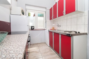 A compact kitchen with white and red cabinets, a built-in oven, and a window providing natural light. - Apartments Lily (Privlaka)