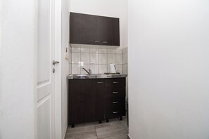 A compact kitchen with dark cabinets, a stainless steel sink, and a white tiled backsplash. - Apartments Lily (Privlaka)