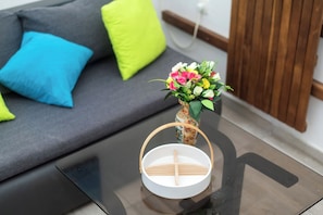 A modern living room with a grey sofa, a glass coffee table, and a small vase with flowers. - Apartments Lily (Privlaka)