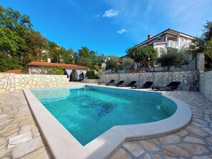 A swimming pool with lounge chairs, stone walls, and a building with a balcony in the background. - Apartments Nono (Crikvenica)