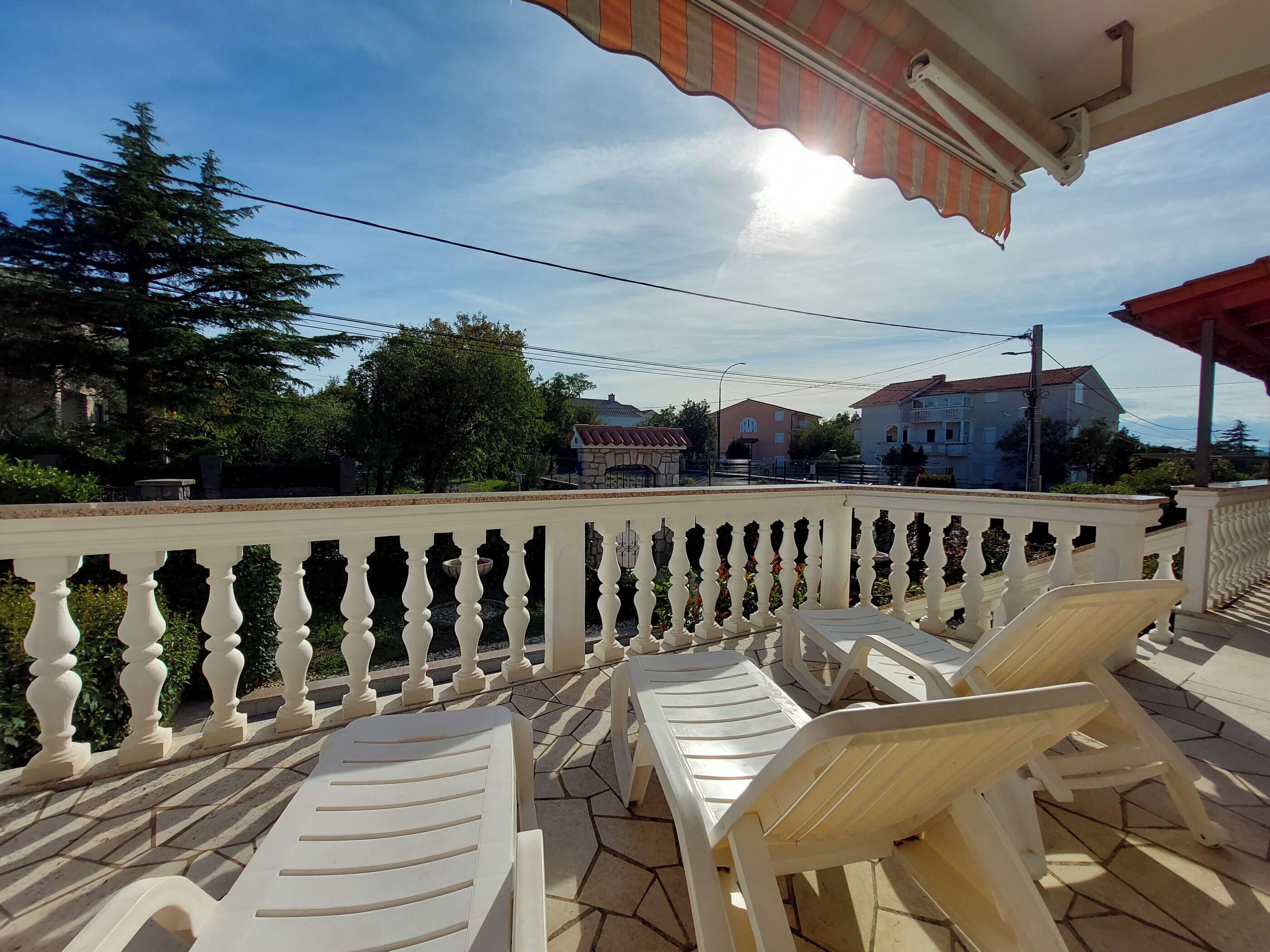 A terrace with white plastic chairs and a white balustrade.