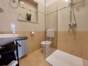 A modern bathroom with a glass shower enclosure, a white toilet, and a sink with a towel rack. - Apartments Nono (Crikvenica)
