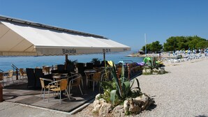 An outdoor seating area with a covered table and chairs, a white awning with "Bavaria BOX" text, and a view of the sea. - Apartments Dusanka (Crikvenica)