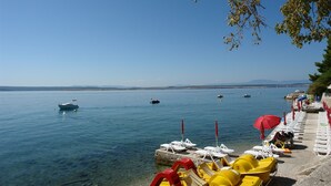 A lakeside beach with clear water, boats, and sun loungers. - Apartments Dusanka (Crikvenica)