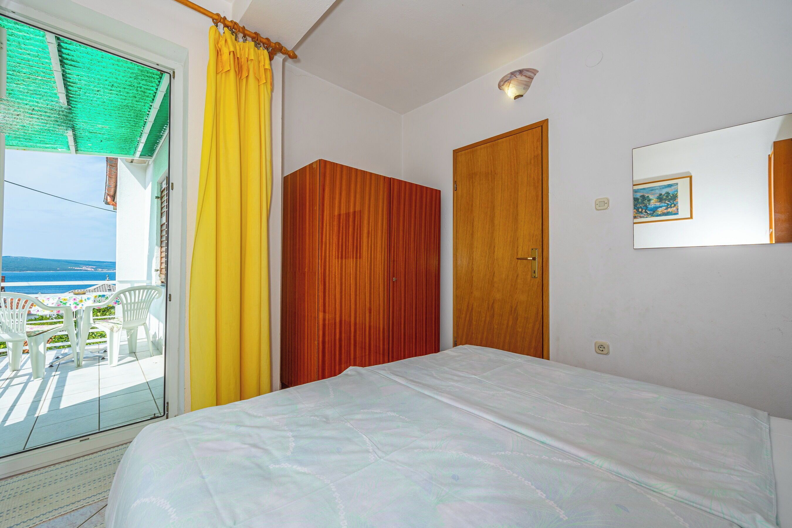 Ein Schlafzimmer mit einem Bett, einem Holzschrank, einer Tür und einem Fenster mit Vorhängen.