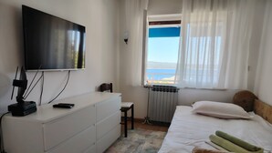A bedroom with a bed, a TV mounted on the wall, a radiator, and a window with curtains. - Apartments Dusanka (Crikvenica)