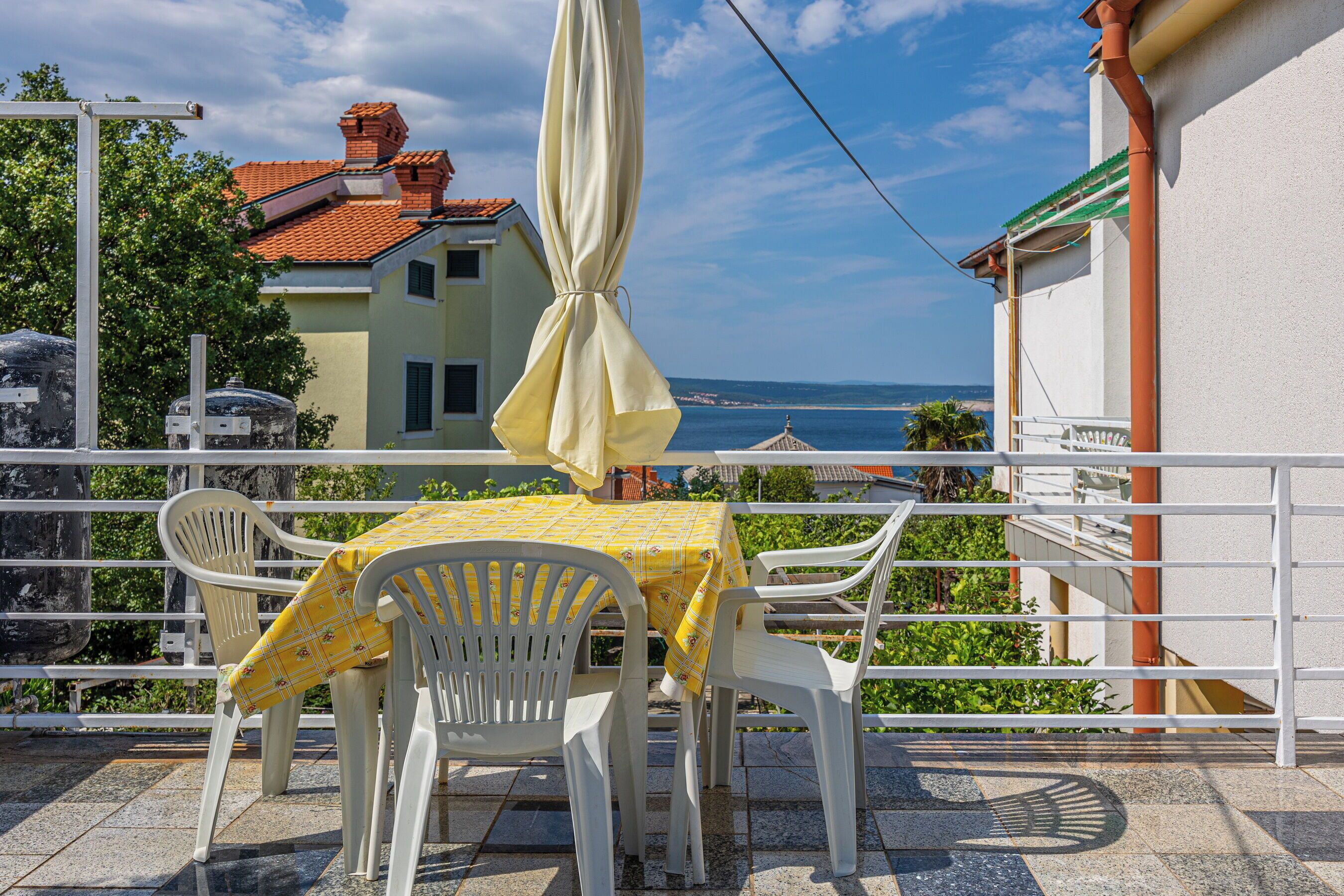 A terrace with a table and chairs, a yellow tablecloth, and a view of the sea.