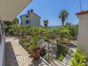 A courtyard with a pergola, potted plants, and a view of a building with a red roof. - Apartments Dusanka (Crikvenica)