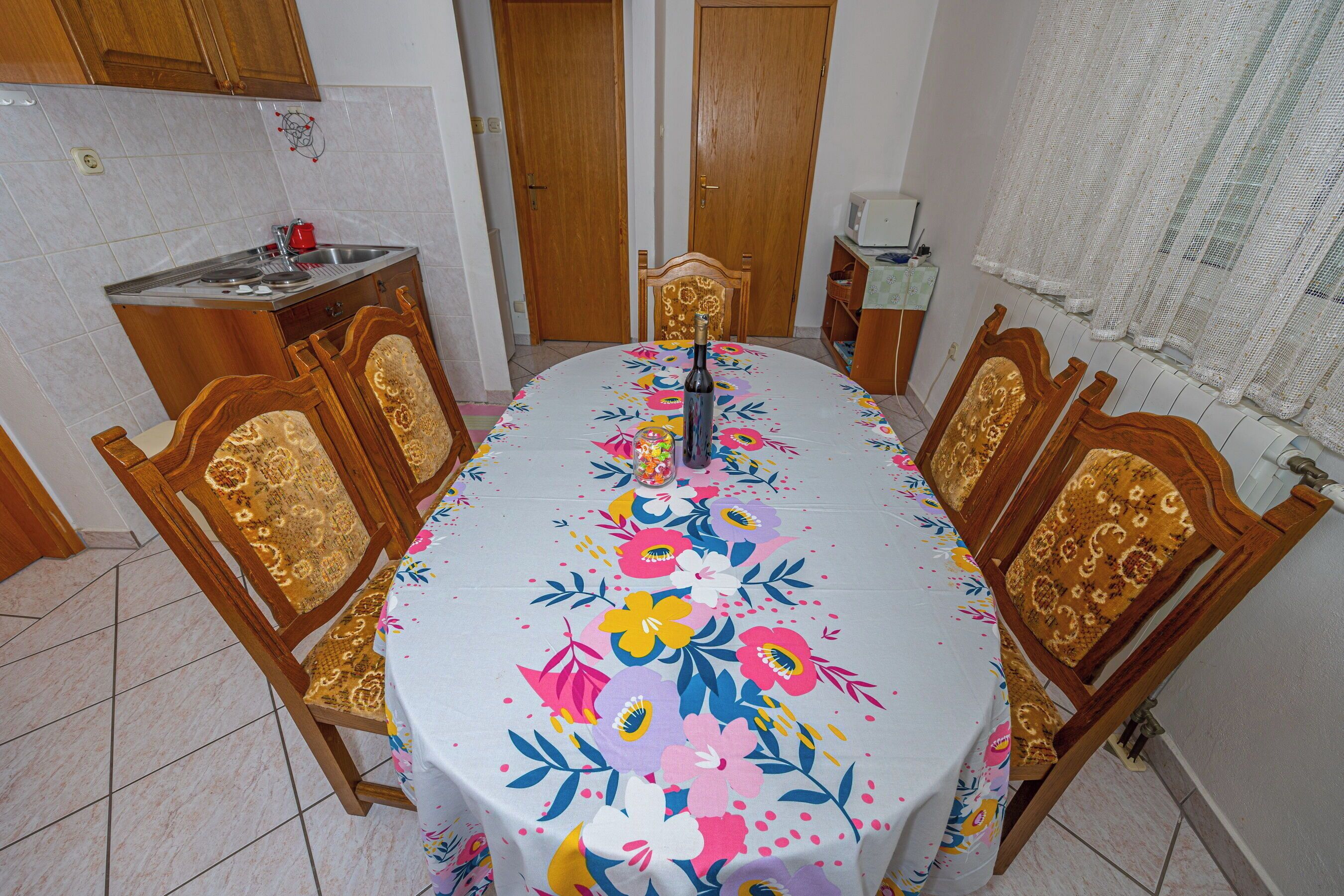 A dining area with a table covered by a floral tablecloth, surrounded by wooden chairs with intricate designs.